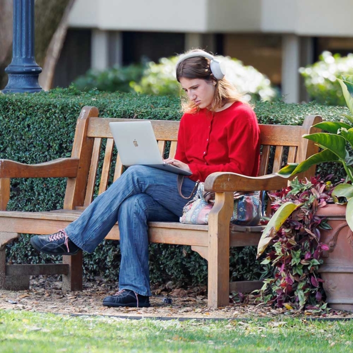 Student on a bench with a laptop and headphones