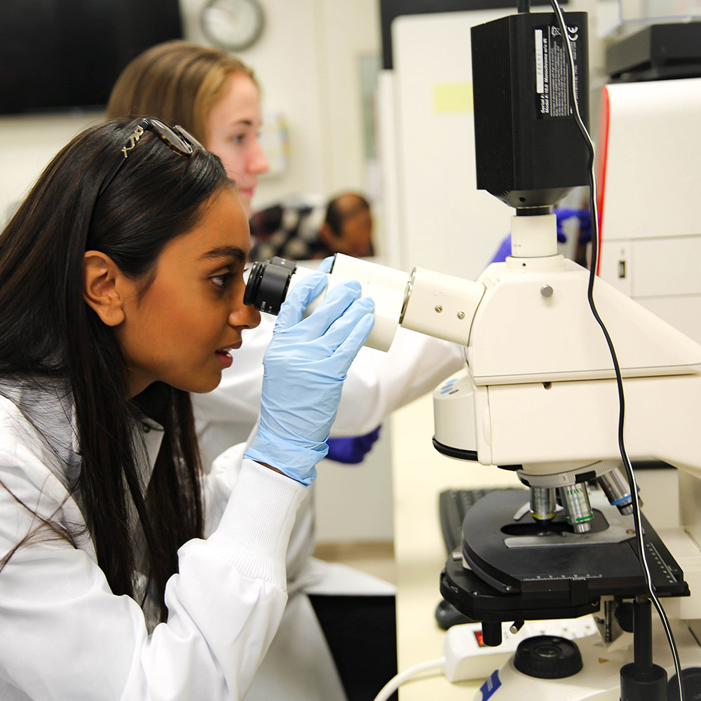 Student in lab coat looking through a microscope