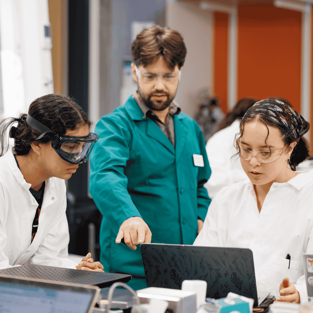 two science students conduct an experiment in a lab with their professor