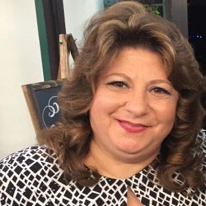 Woman smiling with brown curly hair and a patterned blouse