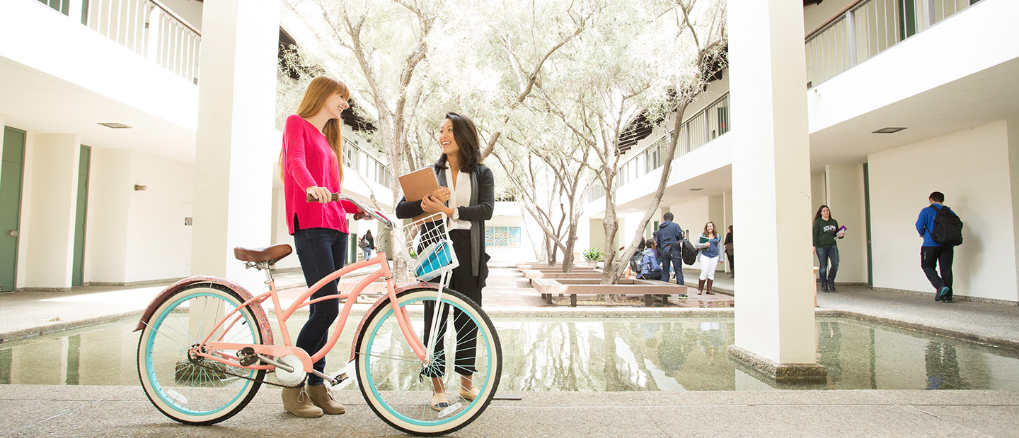 Two students standing talking to each other in Humanities building courtyard