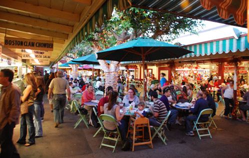 A crowded Original Farmers Market with people eating at tables, standing around, and shopping.