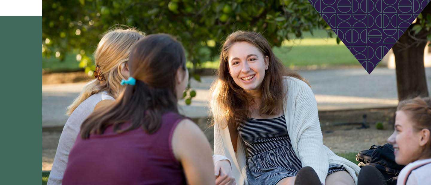 Four students sitting outside talking near an orange tree