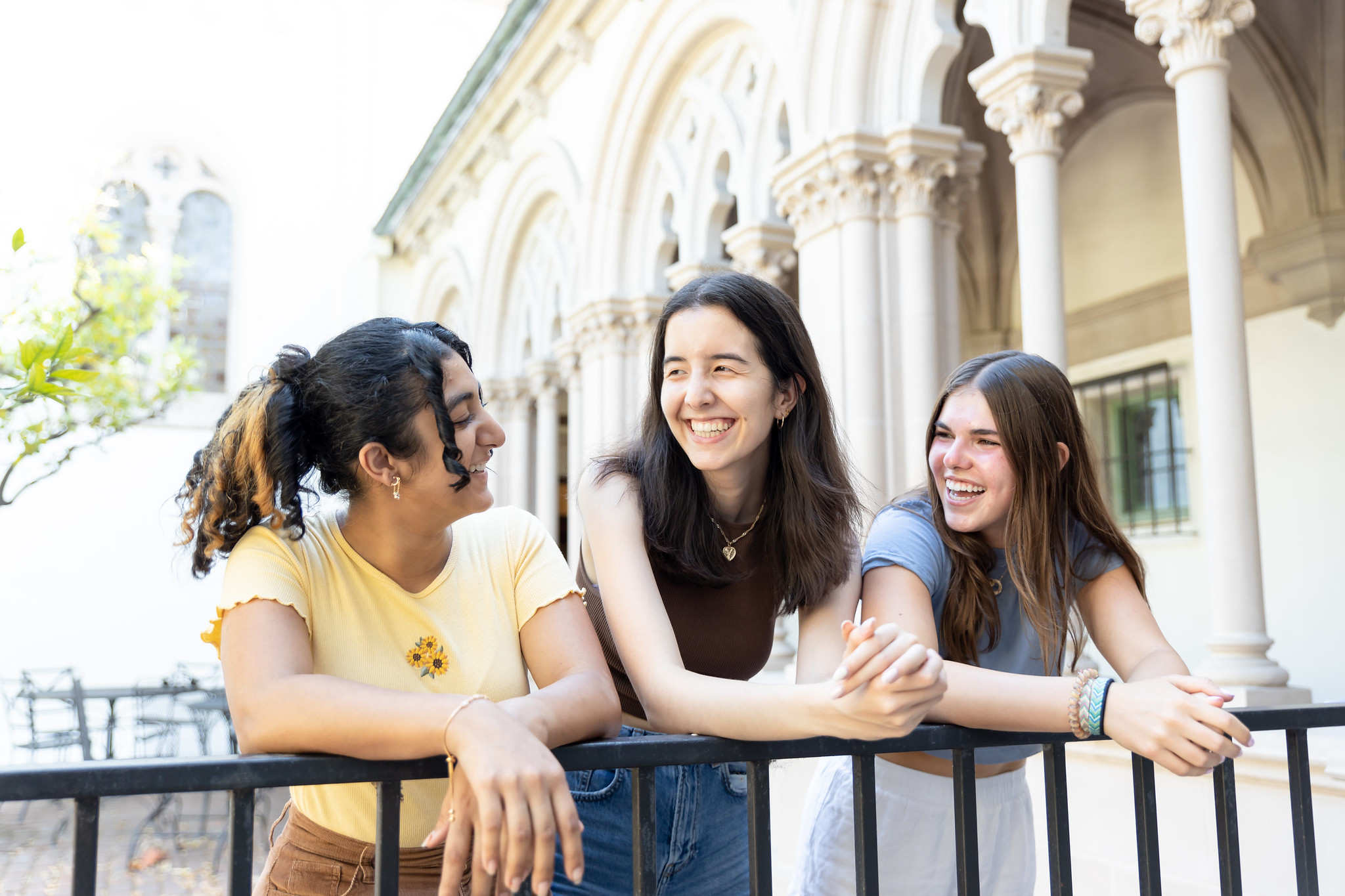 Three students learning against a rail smiling