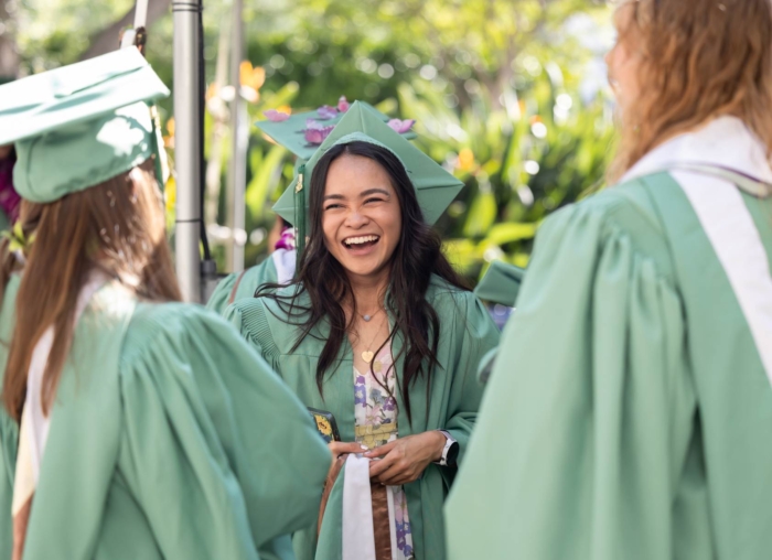 One student in graduation cap and gown smiling to friends