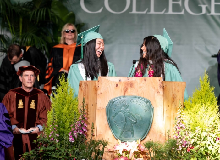 Two students at Commencement podium facing each other and smiling