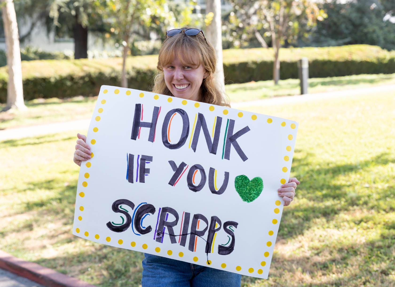 Student smiling carrying sign that reads honk if you love Scripps