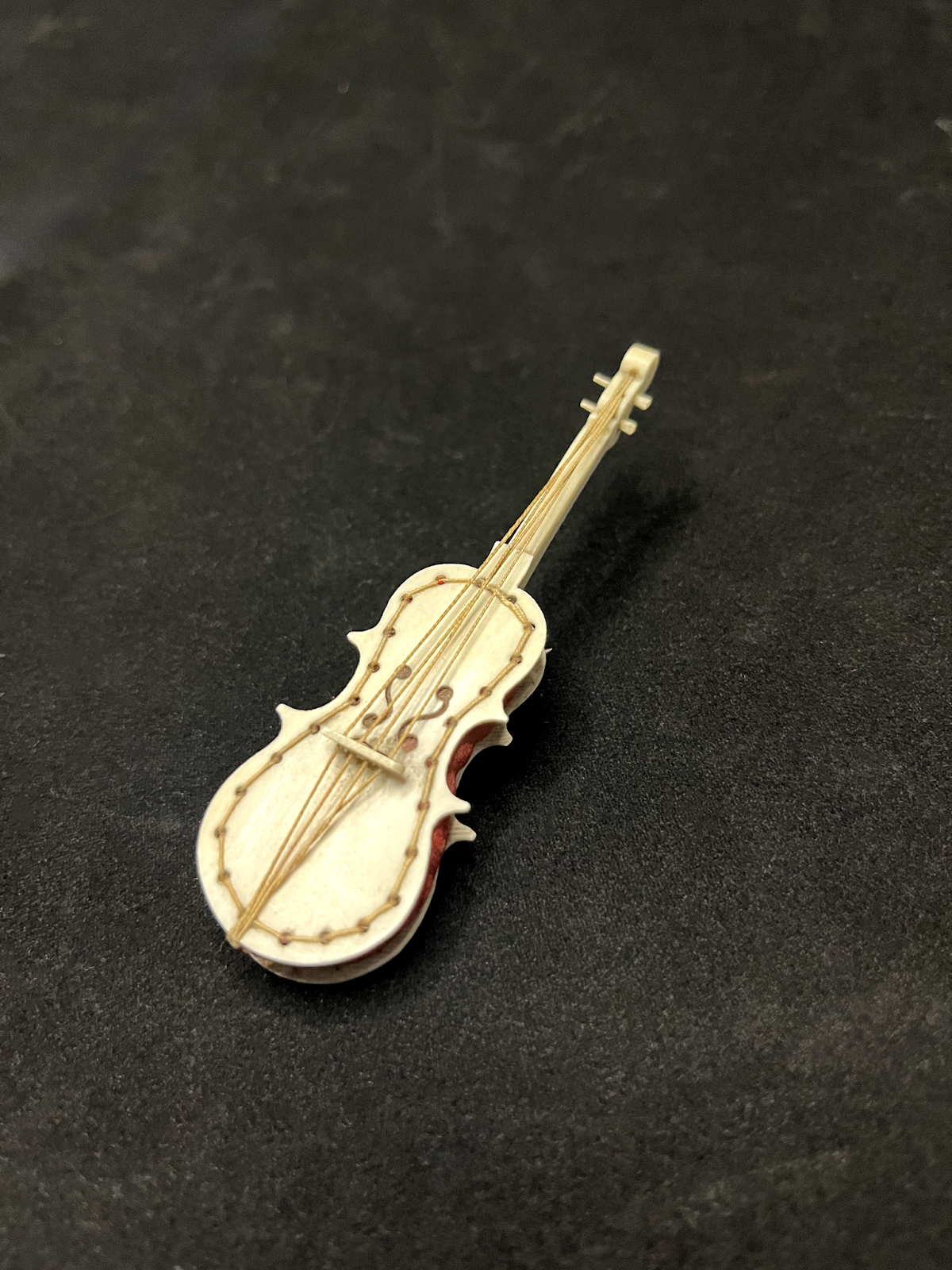 A toy pincushion resembling a violin, still containing pins (not pictured).