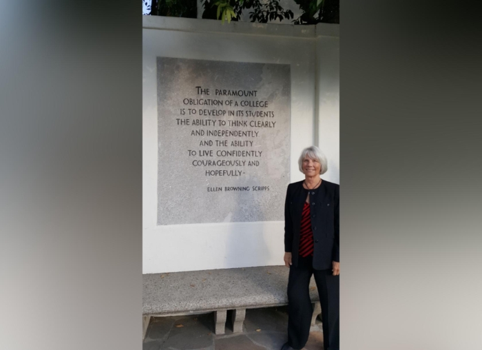Chalan Colby '61 smiles while standing on the Scripps College campus next to a plaque with a quote engraved into the stone by Emily Browning Scripps.