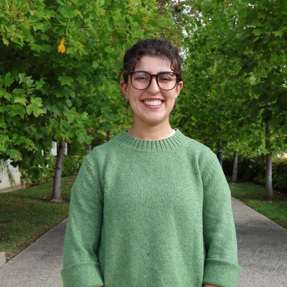 Woman in green shirt stands on path with trees behind her