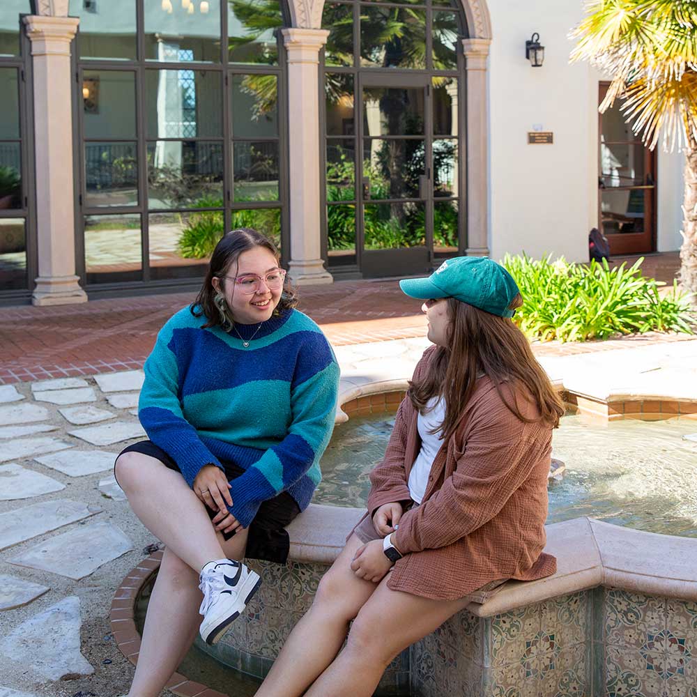 Two students sitting near a fountain in a courtyard of Schow Hall
