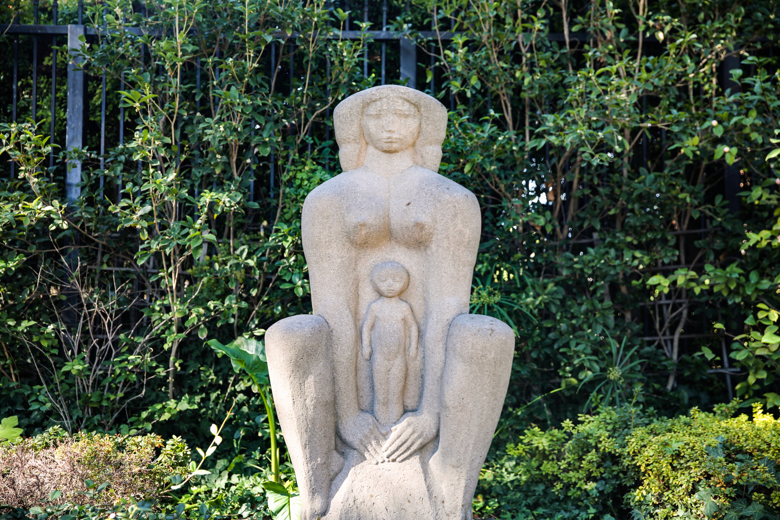 A softly carved stone statue of a sitting woman cradles the stone figure of a child