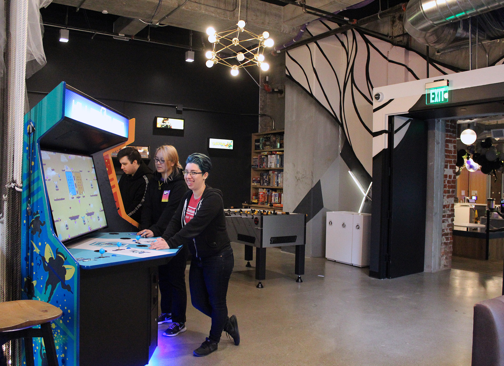 Three people playing arcade games in a game room.