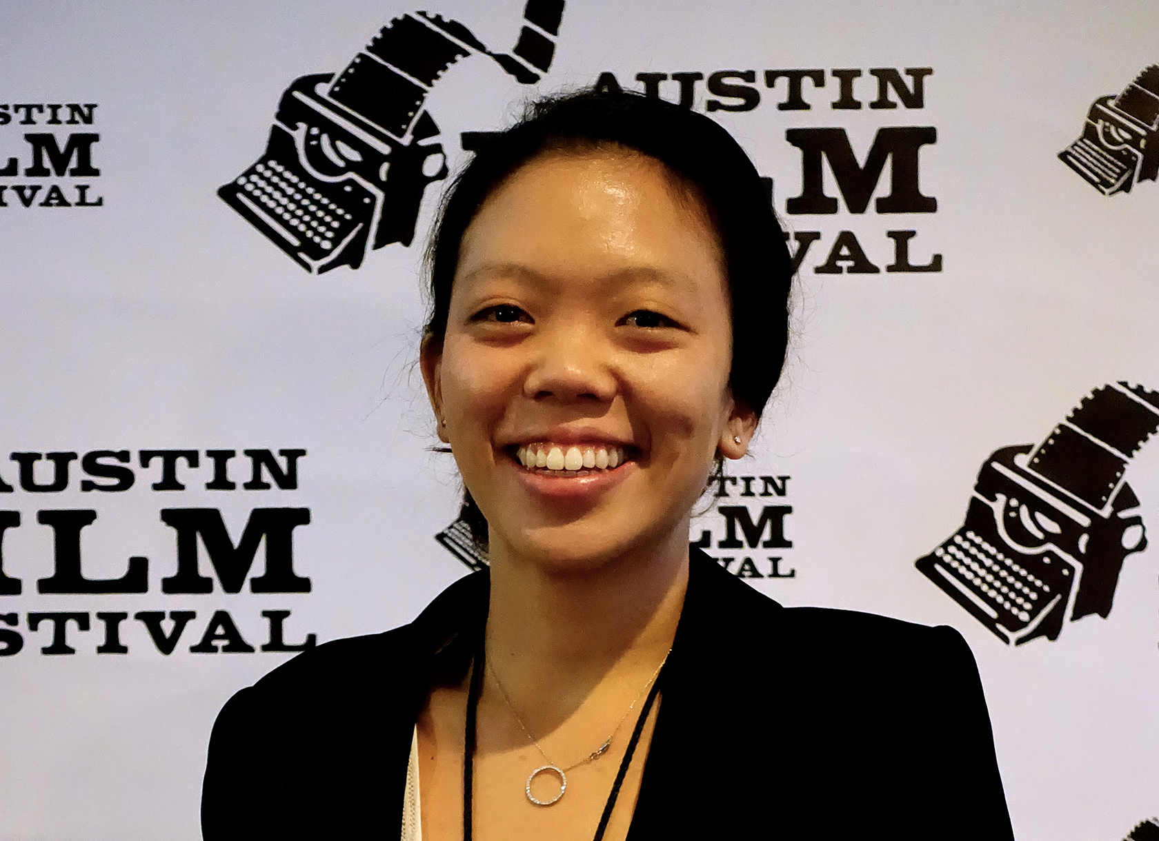 A headshot of a smiling Asian woman wearing a black blazer at a film festival. 