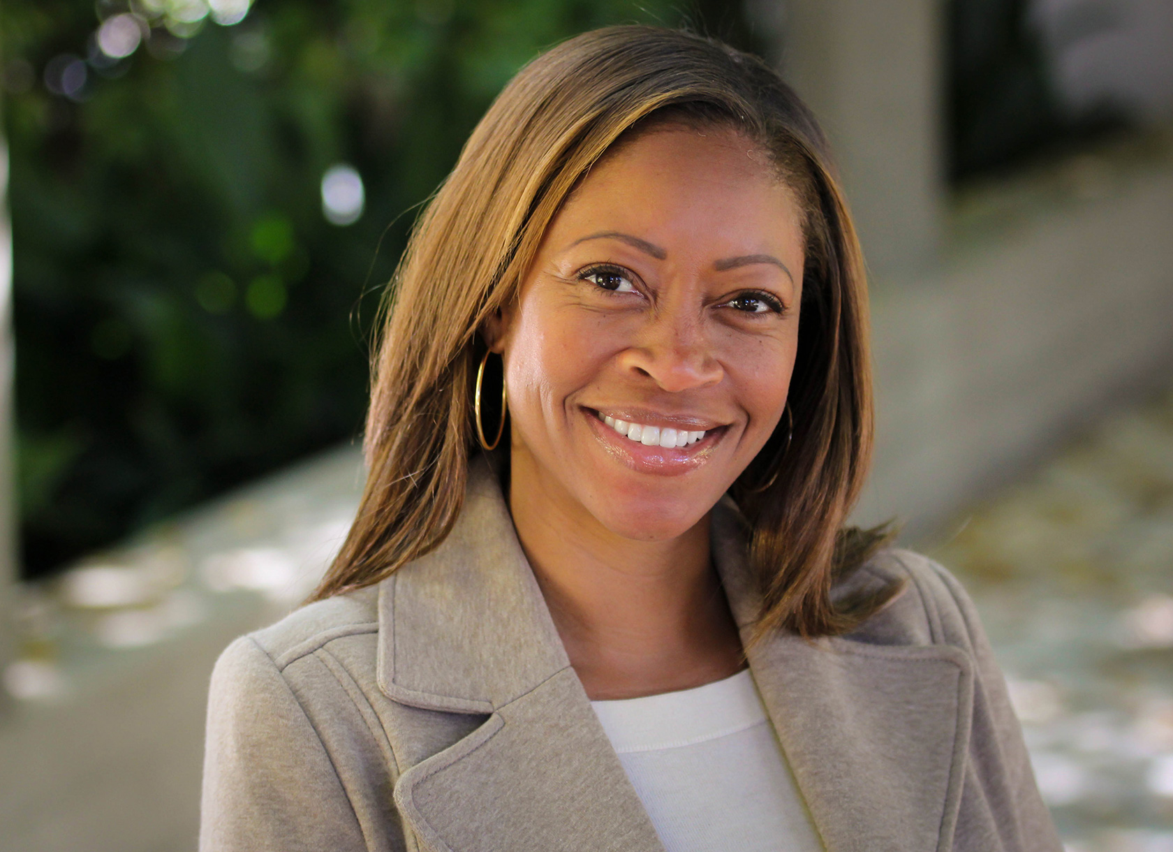 A headshot of a black woman with shoulder-length brown hair wearing a gray blazer.