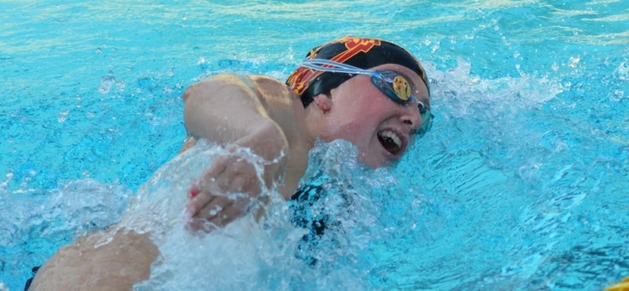 A young woman wearing goggles and a swim cap swimming in a pool.