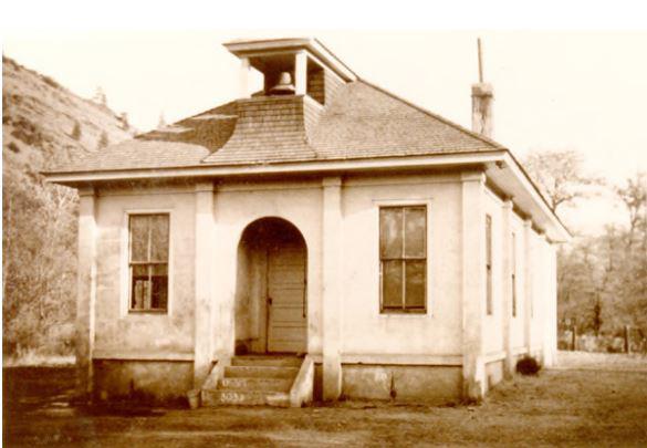 A black and white image of a small schoolhouse with a bell.