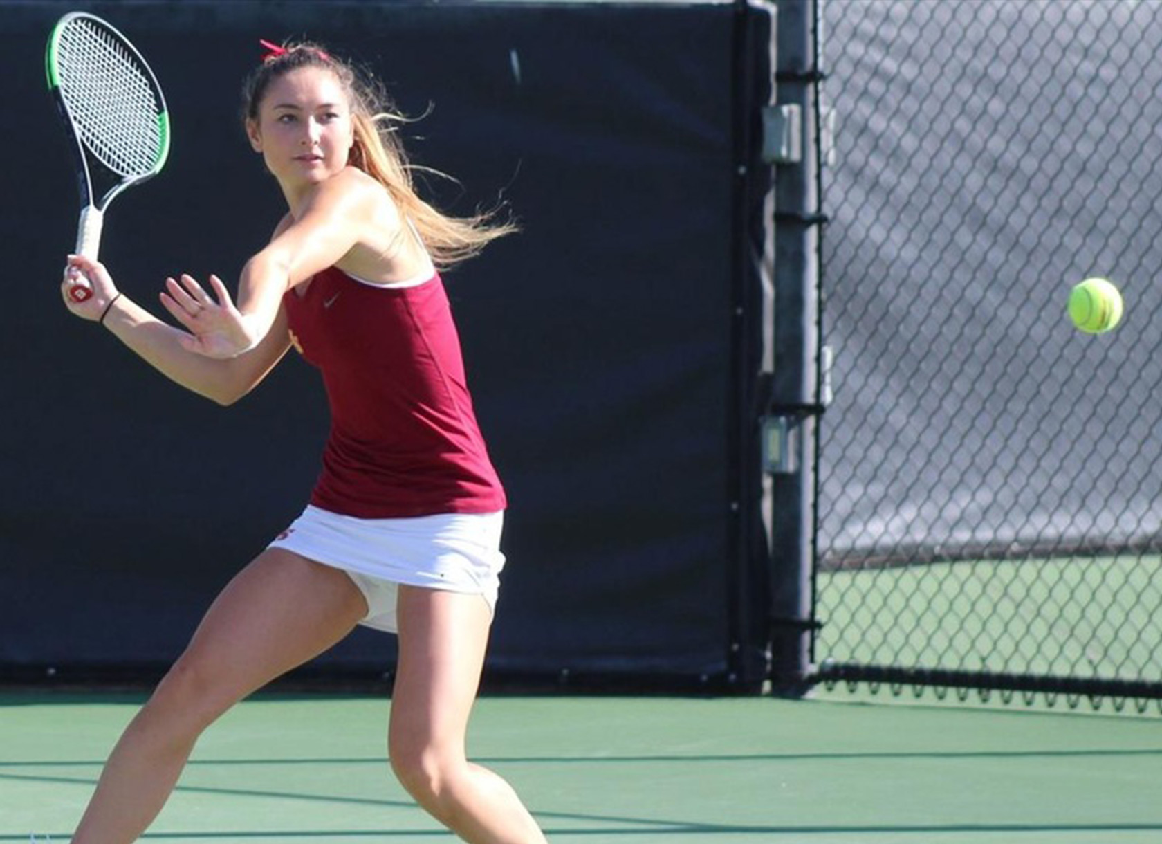 A student wearing a tennis uniform playing tennis on a tennis court.