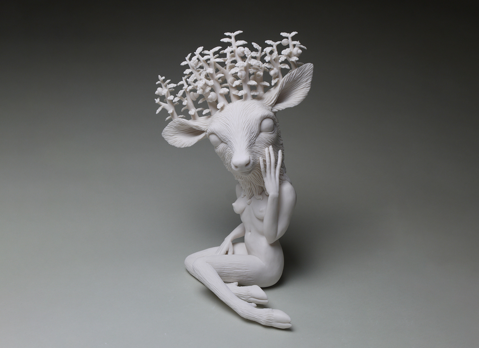 Ceramic statue of a fawn with trees for horns and the body of a human female.