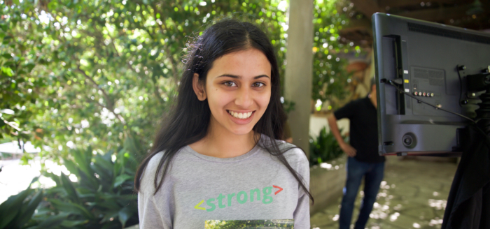 A young South Asian woman with long black hair wearing a shirt that says '<strong>'