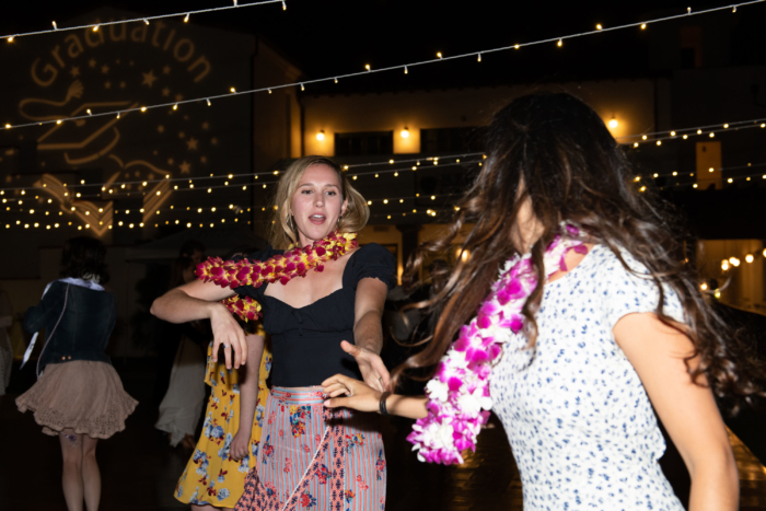 Two young woman in formal clothes and floral leis dancing outside at night.