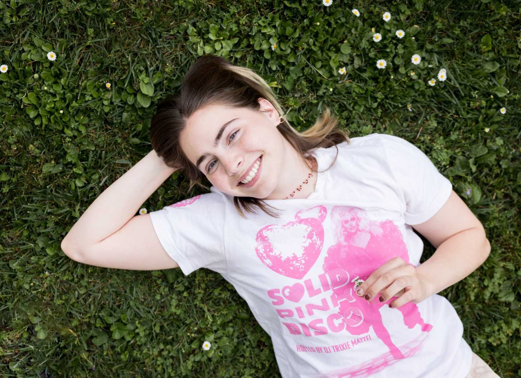 Ellie Ringness, a senior from the Class of 2025, smiles while laying in the grass, surrounded by small fllowers