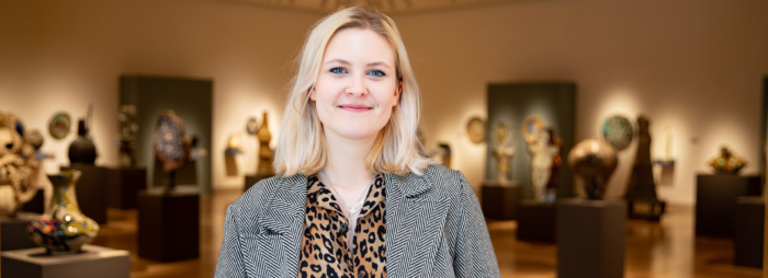 A young white woman with blond hair wearing a blazer and leopard print shirt smiling in an art gallery.