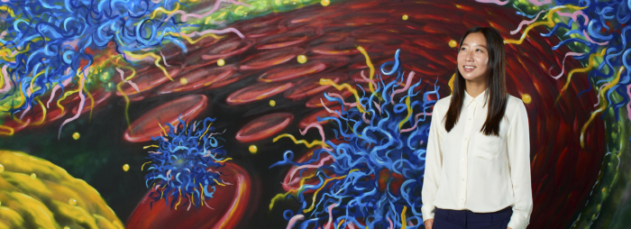 An Asian woman in a white dress shirt looking up against a background image of blood cells and other biological things.