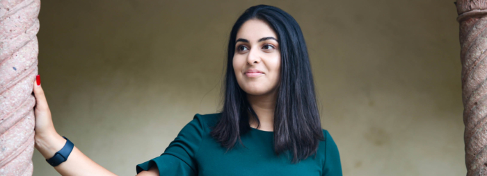 A young South Asian woman with black hair and a green shirt smiling and looking to the left.