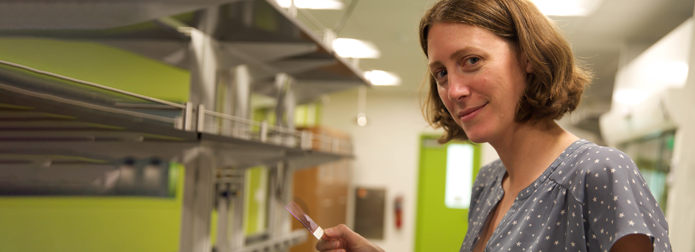 A white woman with short light brown hair holding a microscope slide in a science lab.