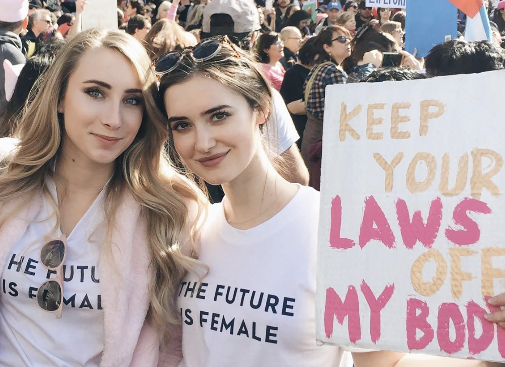 Two young white women at a protest posing with a sign that says 'Keep your laws off my body.'
