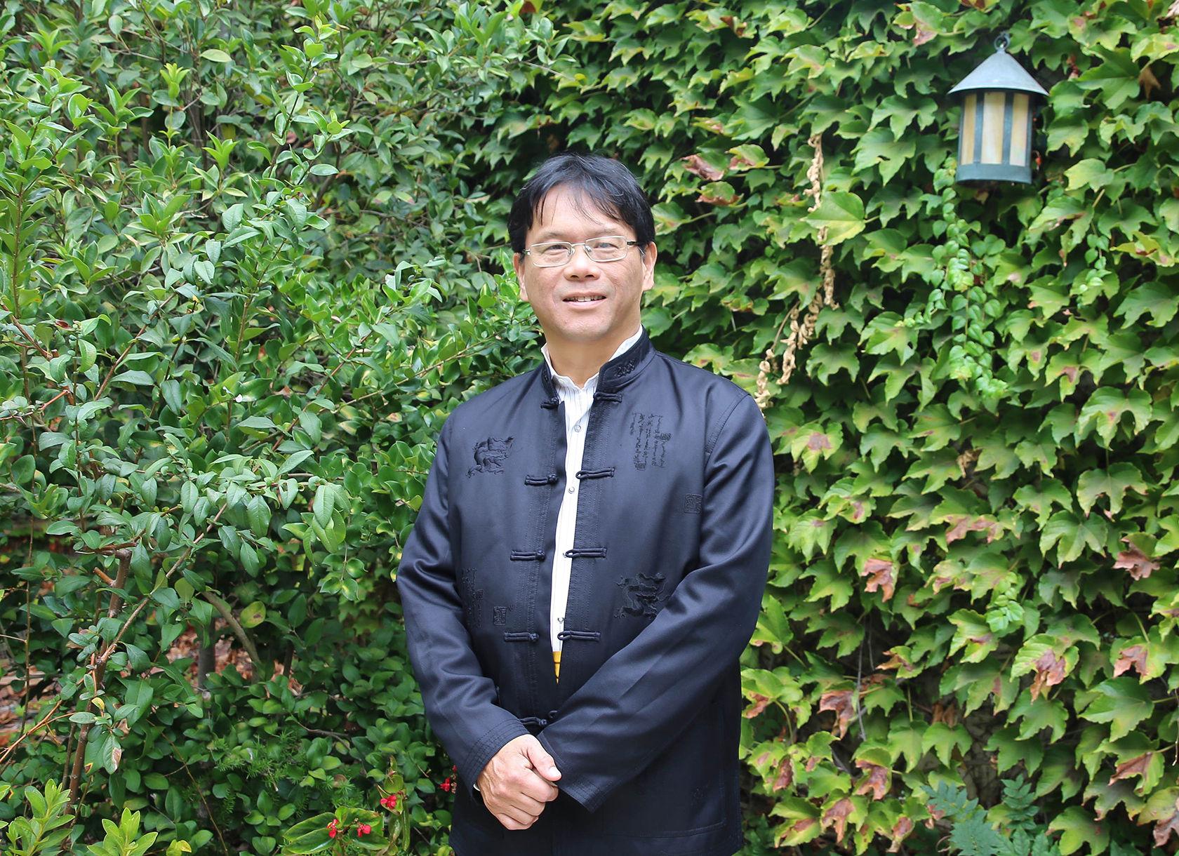 An Asian man with black hair wearing glasses and black traditional clothing.