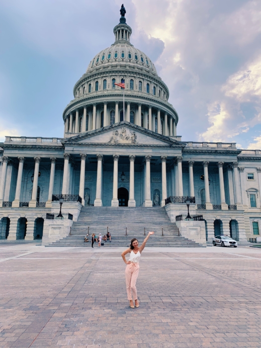 A young white woman in a white tank top and pink pants posing on Capital Hill.