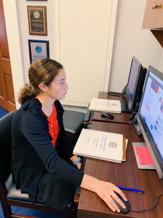 A young white woman with brown hair and wearing professional clothing working at a desktop computer.