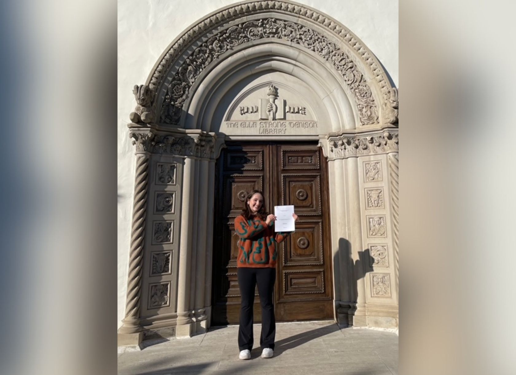 Scripps College student Julia Cox '23 holds up her thesis in front of the Denison Library doors