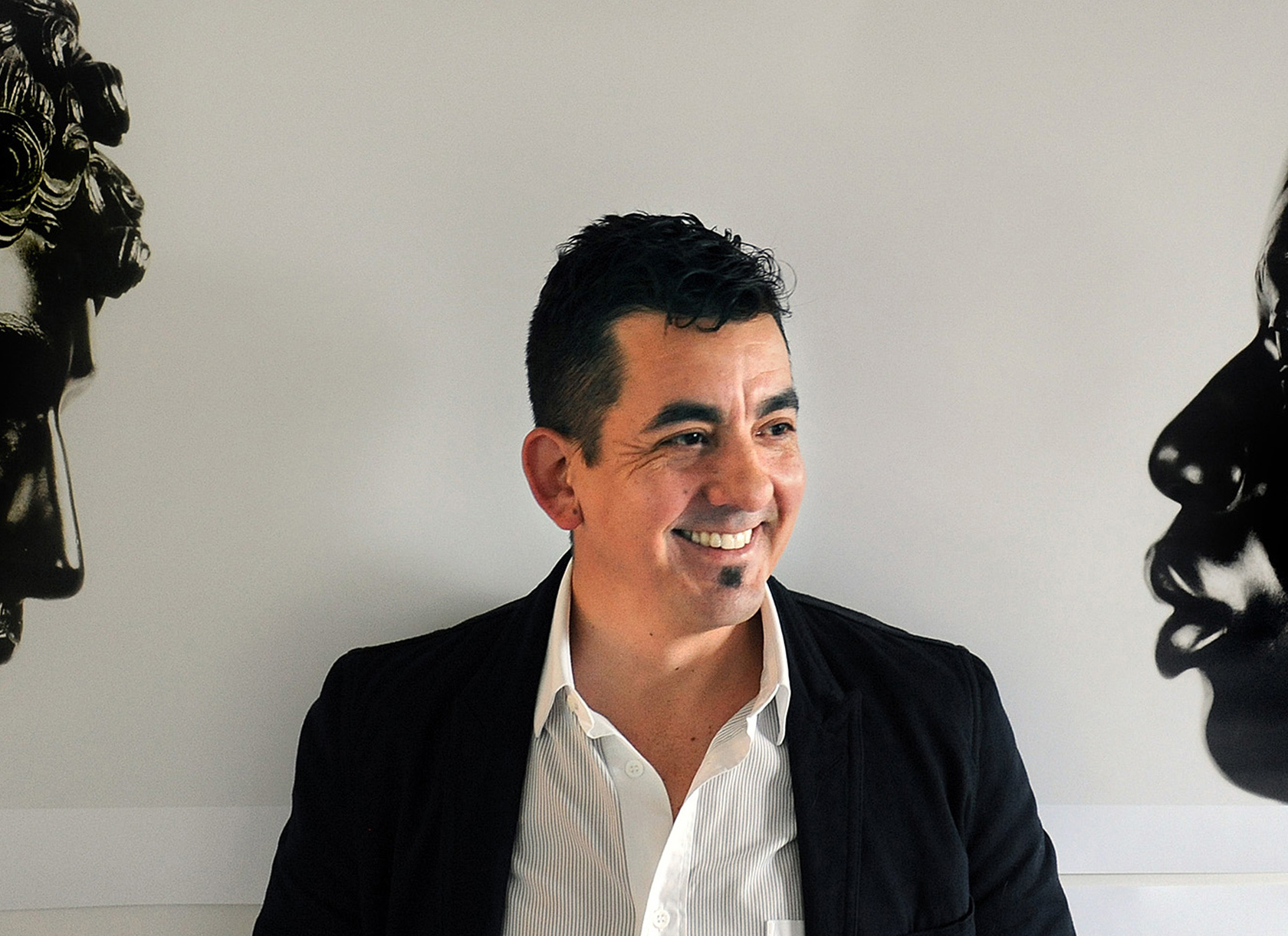 A Hispanic man wearing a white shirt and black blazer smiling and gazing to the side.