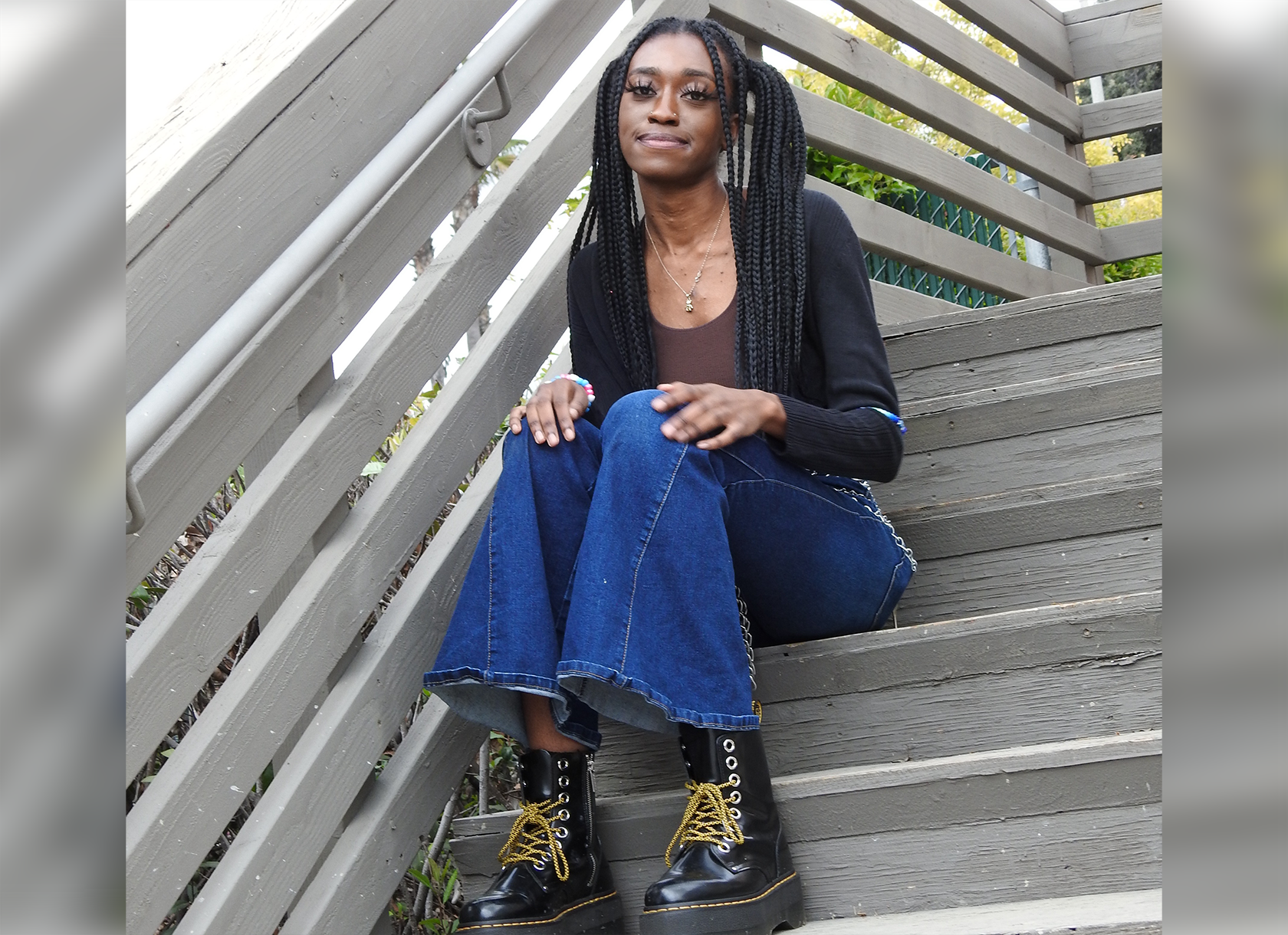 Photograph of Kushnerniva Laurent '24, a Black woman with long hair, wearing jeans and sitting on wooden stairs.