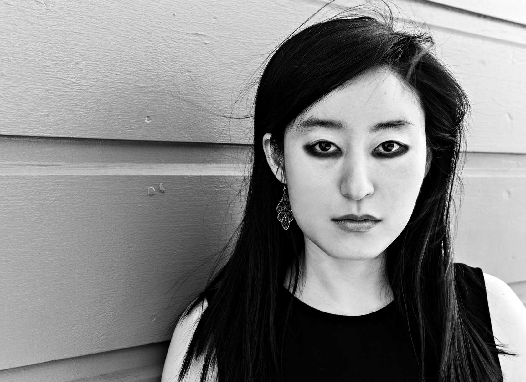 A black and white headshot of a young Asian woman with long black hair and black eyeliner.