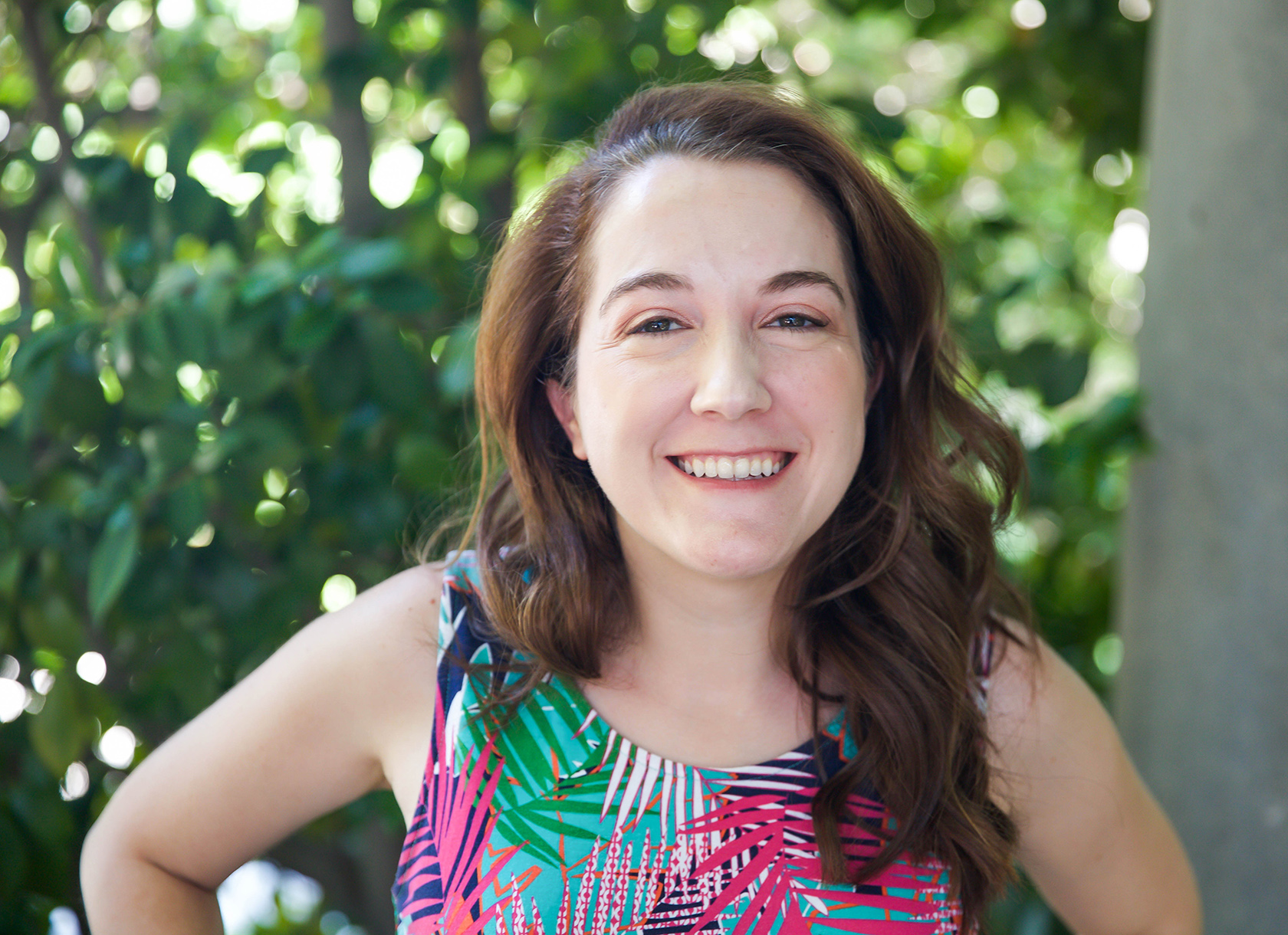 Woman with shoulder-length brown hair and flowered dress smiles at the camera