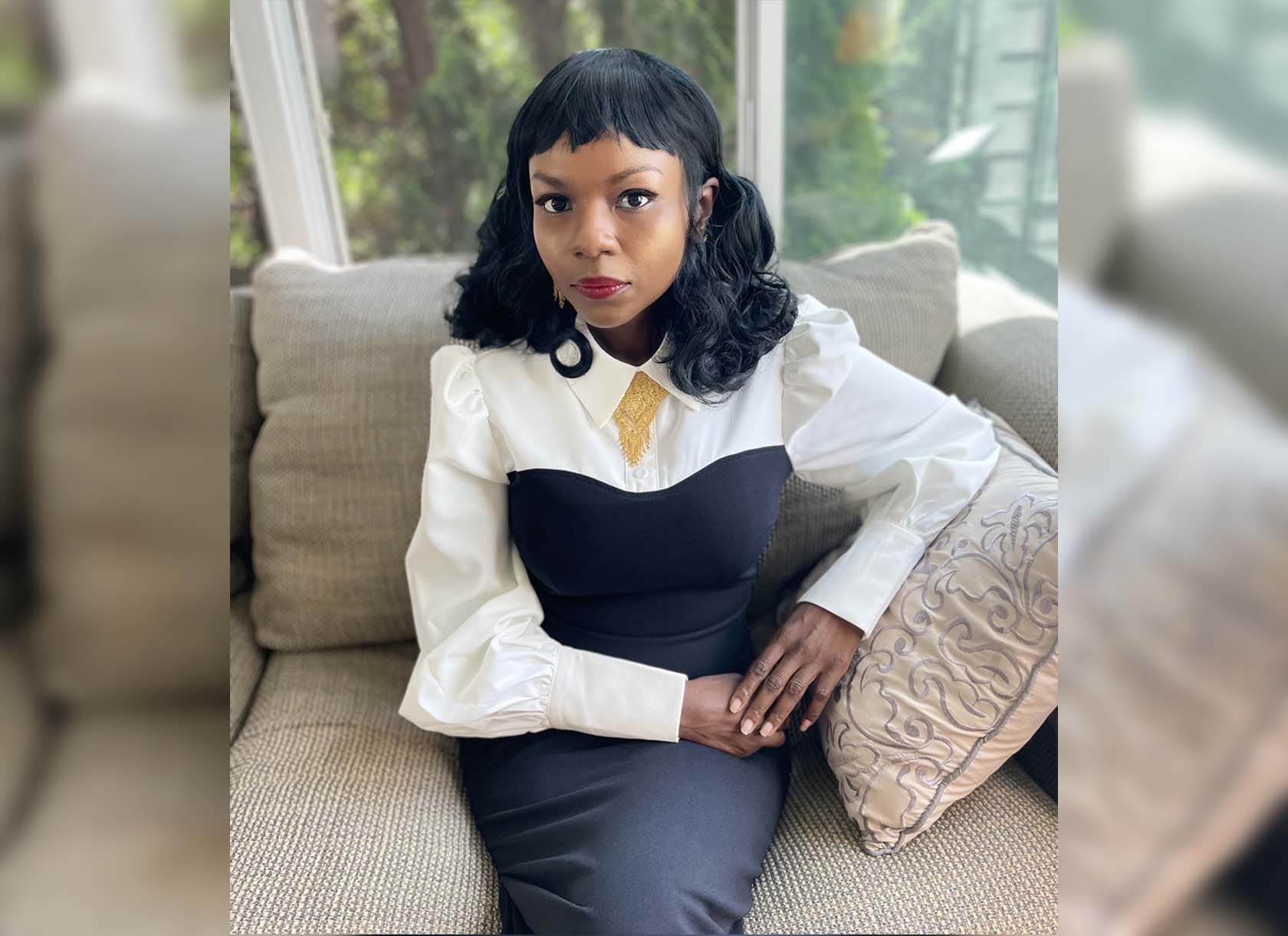 A photograph of Mary-Alice Daniel, seated. She is a Black woman with shoulder-length hair wearing a black and white long-sleeved dress.