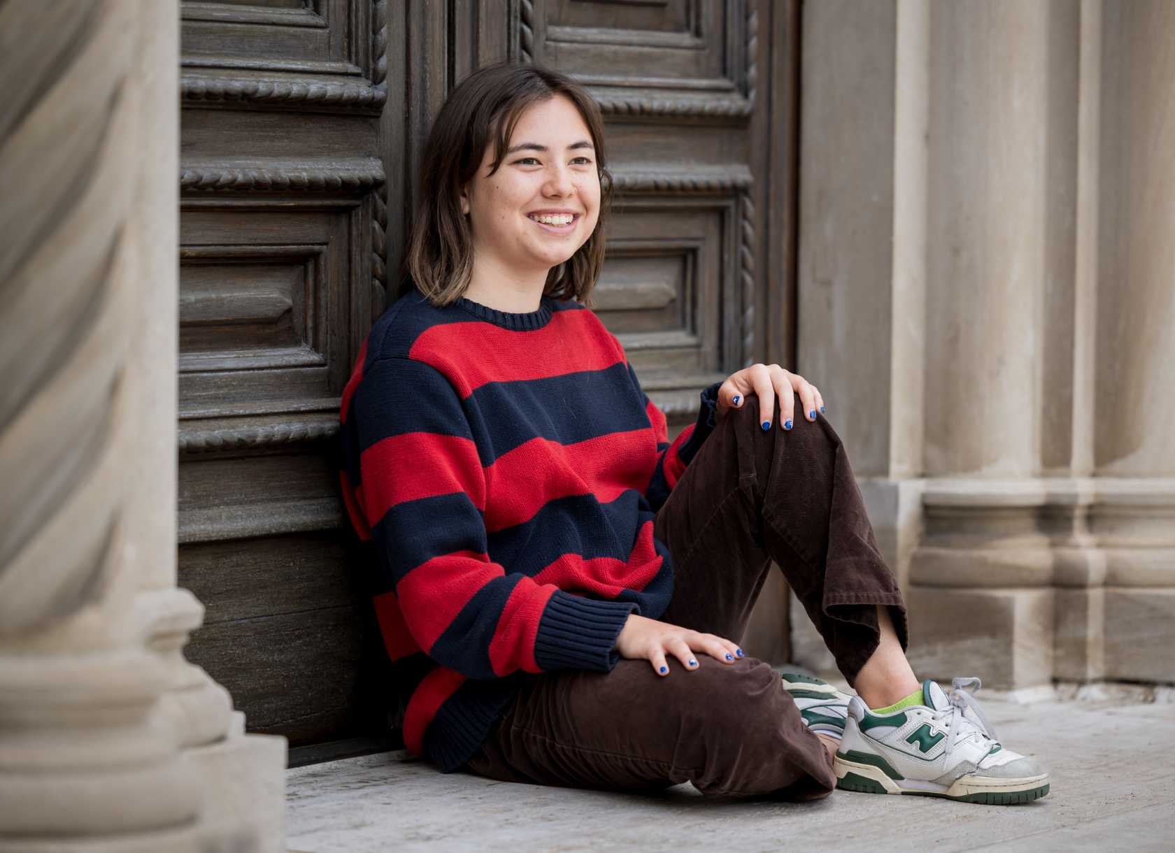 Melina Durre, a senior from the Class of 2025, smiles while seated in front of the Denison Library doors
