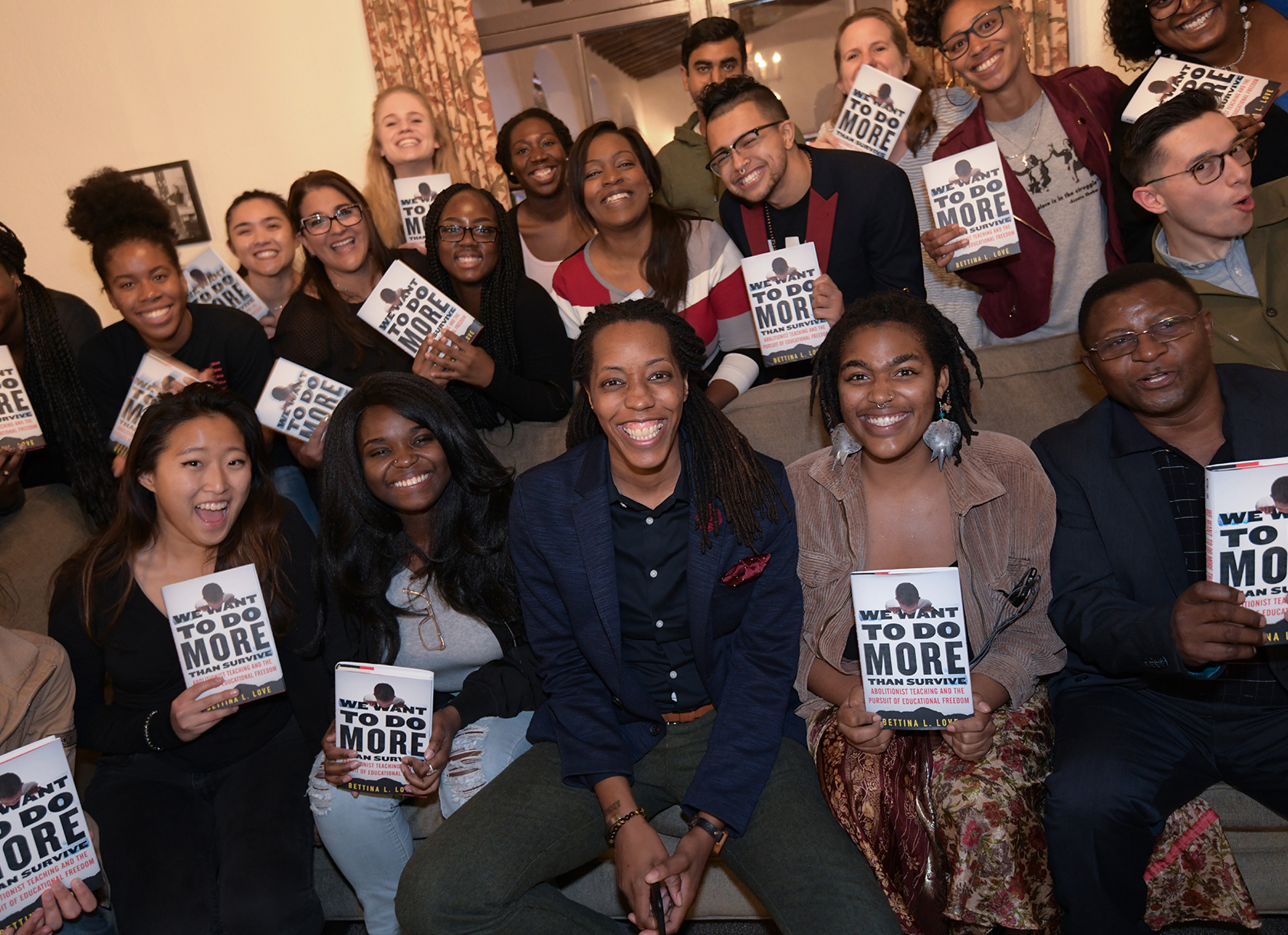 A group of students each holding a book posing with a black woman.