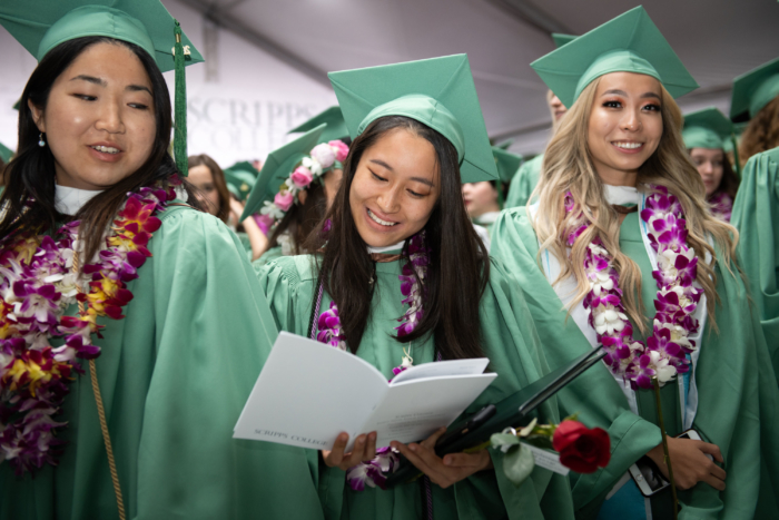 Three young women wearing green graduation caps and gowns and wearing colorful leis.
