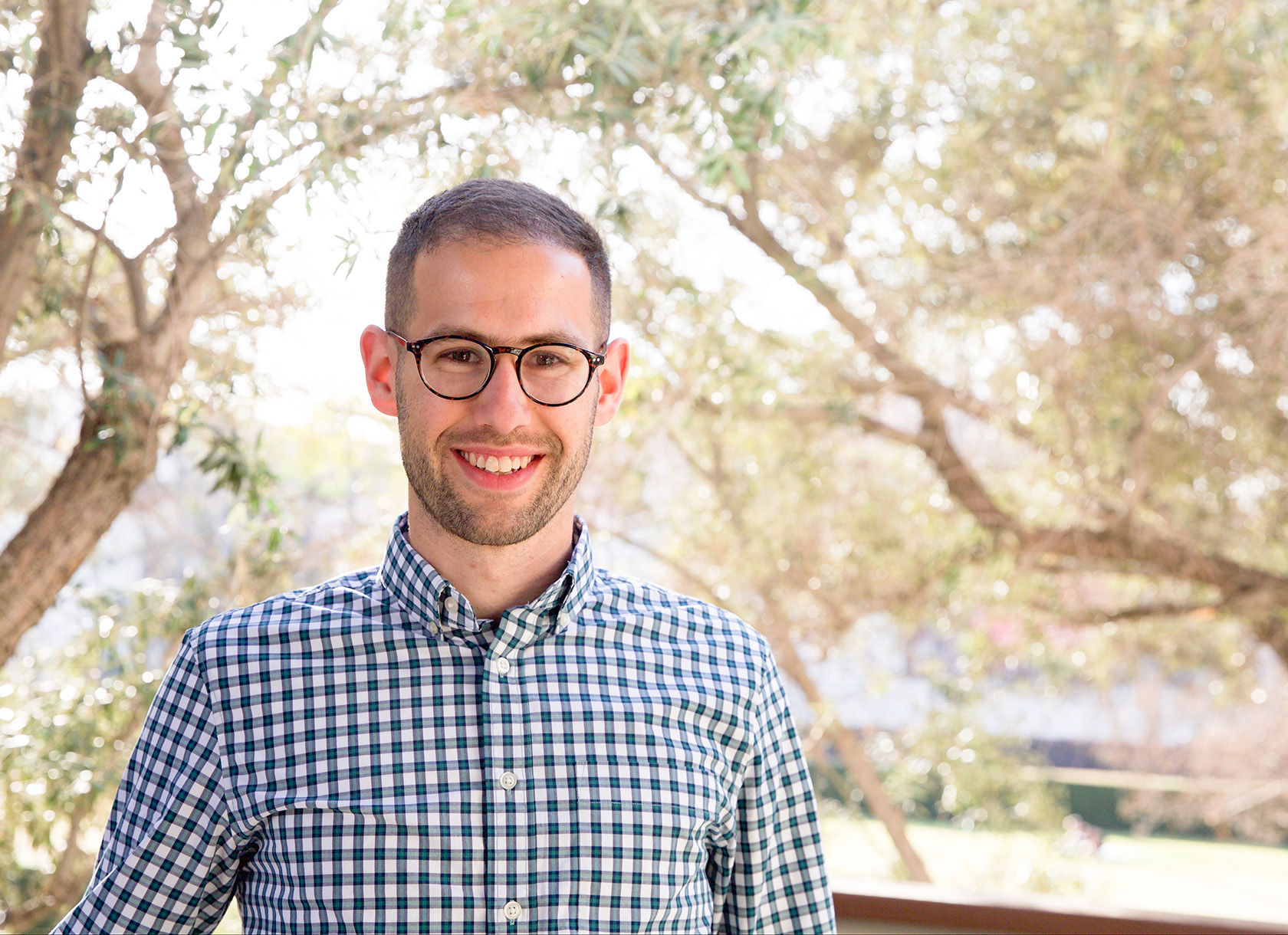 A portrait photo of a white man with glasses and a plaid shirt smiling at the camera.