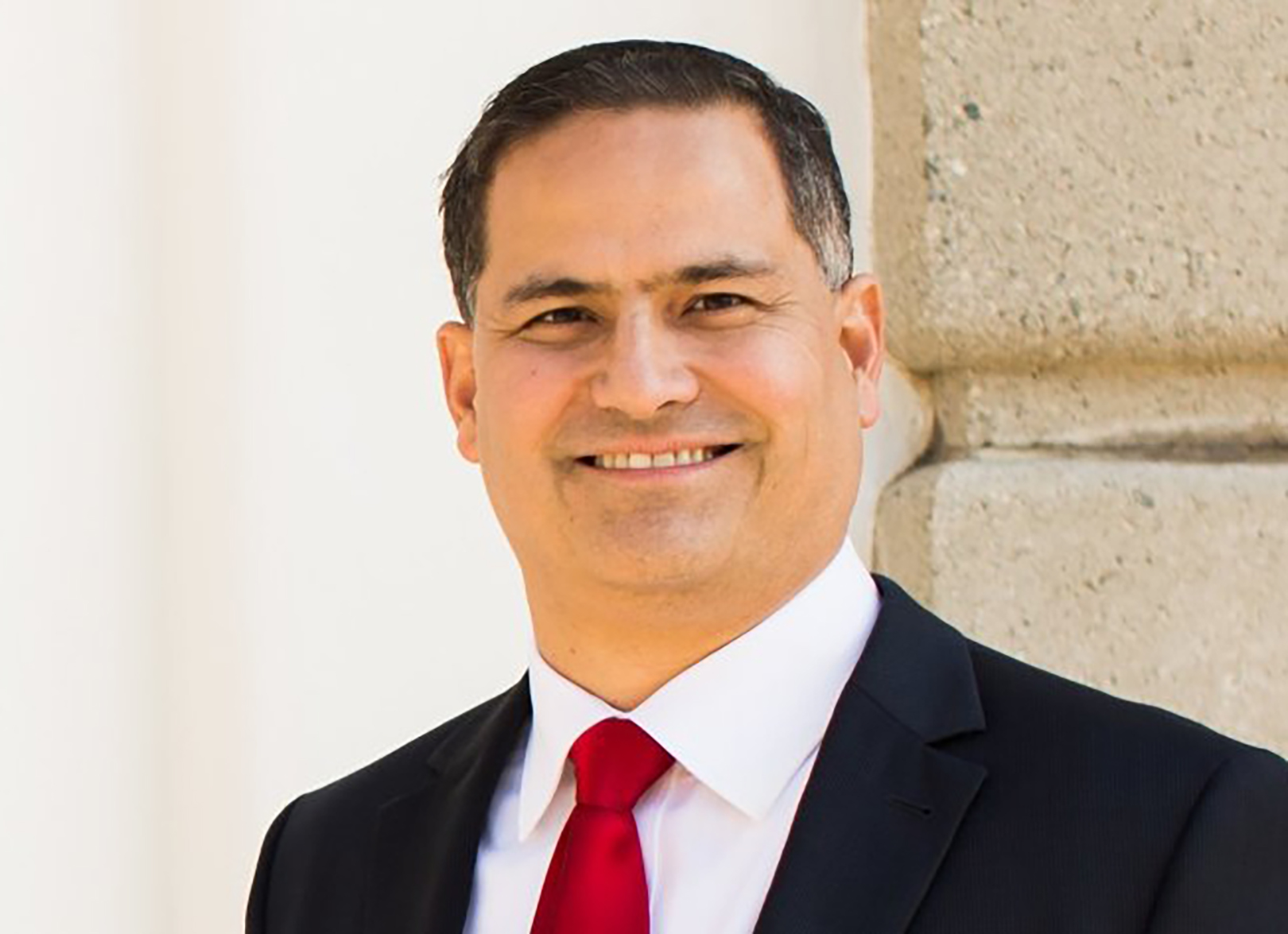 A headshot of a smiling white man wearing a black tuxedo and red tie.