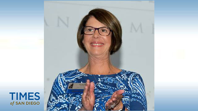 A woman with short brown hair. glasses, and a nametag wearing glasses and looking up while clapping in a photo from the Times of San Diego.