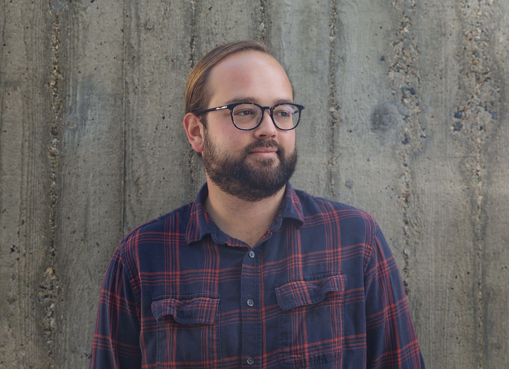 Bearded white man wearing plaid shirt and glasses looks to the right