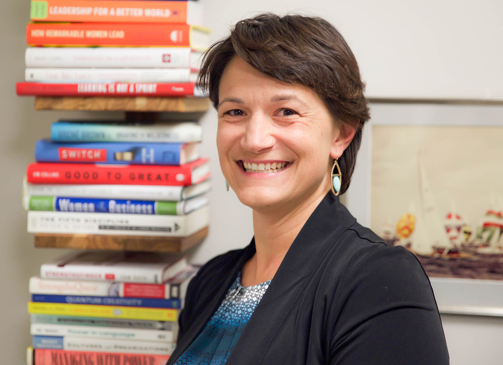 A white woman with short brown hair who is wearing a blazer and dress shirt and smiling.