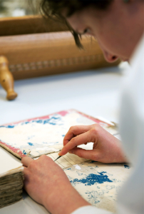 A conservator removes remnants of old end sheets from a book's cover boards. Photo by Martha Benedict.