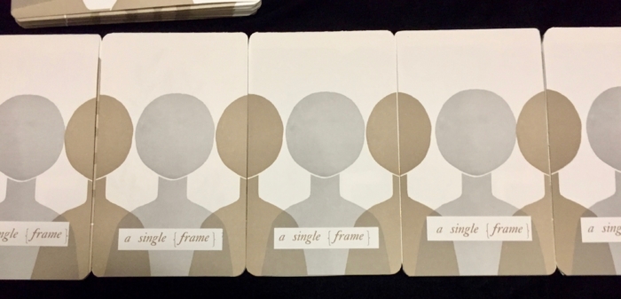 Copies of a handmade book lined up next to each, with shoulder-up renderings of black and gray human figures on the covers. 